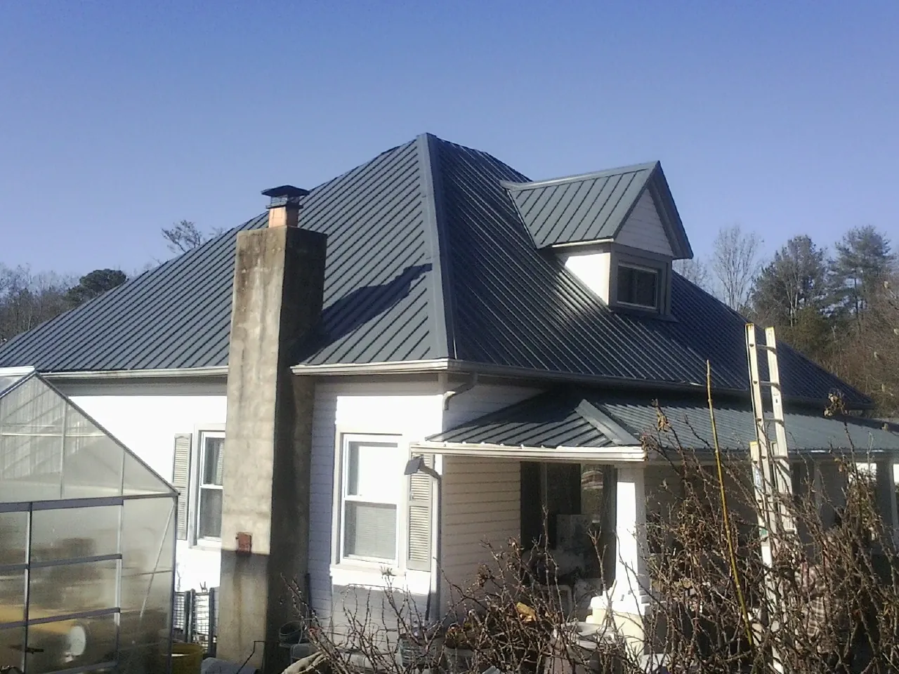 Dark blue standing seam metal roof on a white farmhouse with dormer — Slate & Tile Roof Repair by Roofing Brothers in Chinquapin