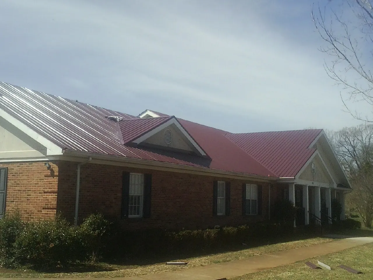 Red metal roof with gabled entries on a long brick building, from a Hail Damage Roof Repair job in Chinquapin