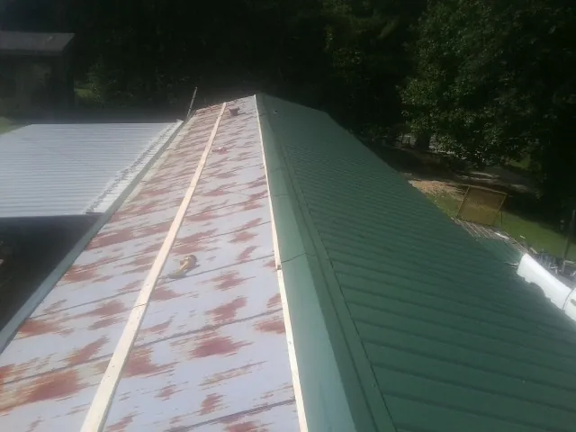 Old rusted panels beside newly installed green metal roofing — Wind Damage Roof Repair by Roofing Brothers in Chinquapin