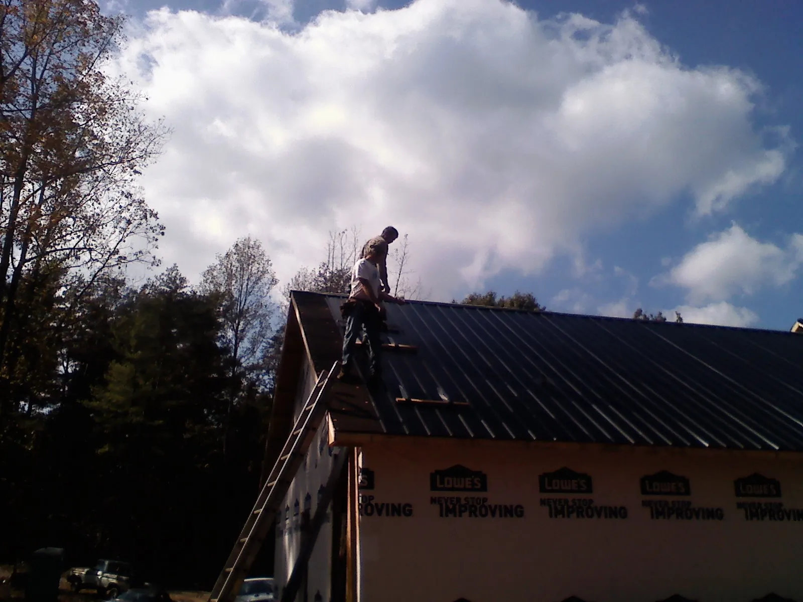 Roofer fastening dark metal panels high against a cloudy sky, from a Roof Inspection job in Chinquapin