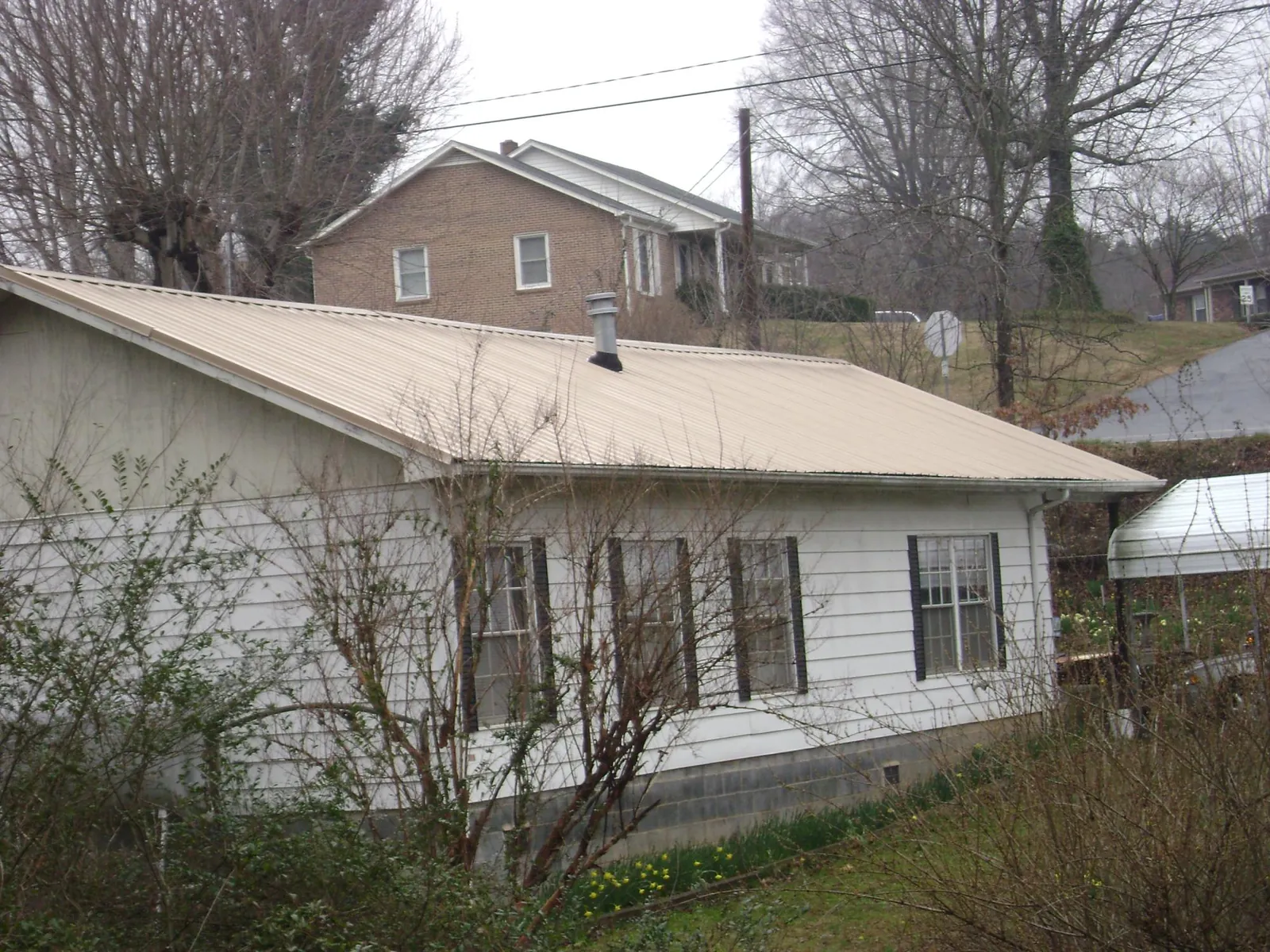 Tan metal roof on a white sided house set into a hillside — Commercial Roofing by Roofing Brothers in Chinquapin