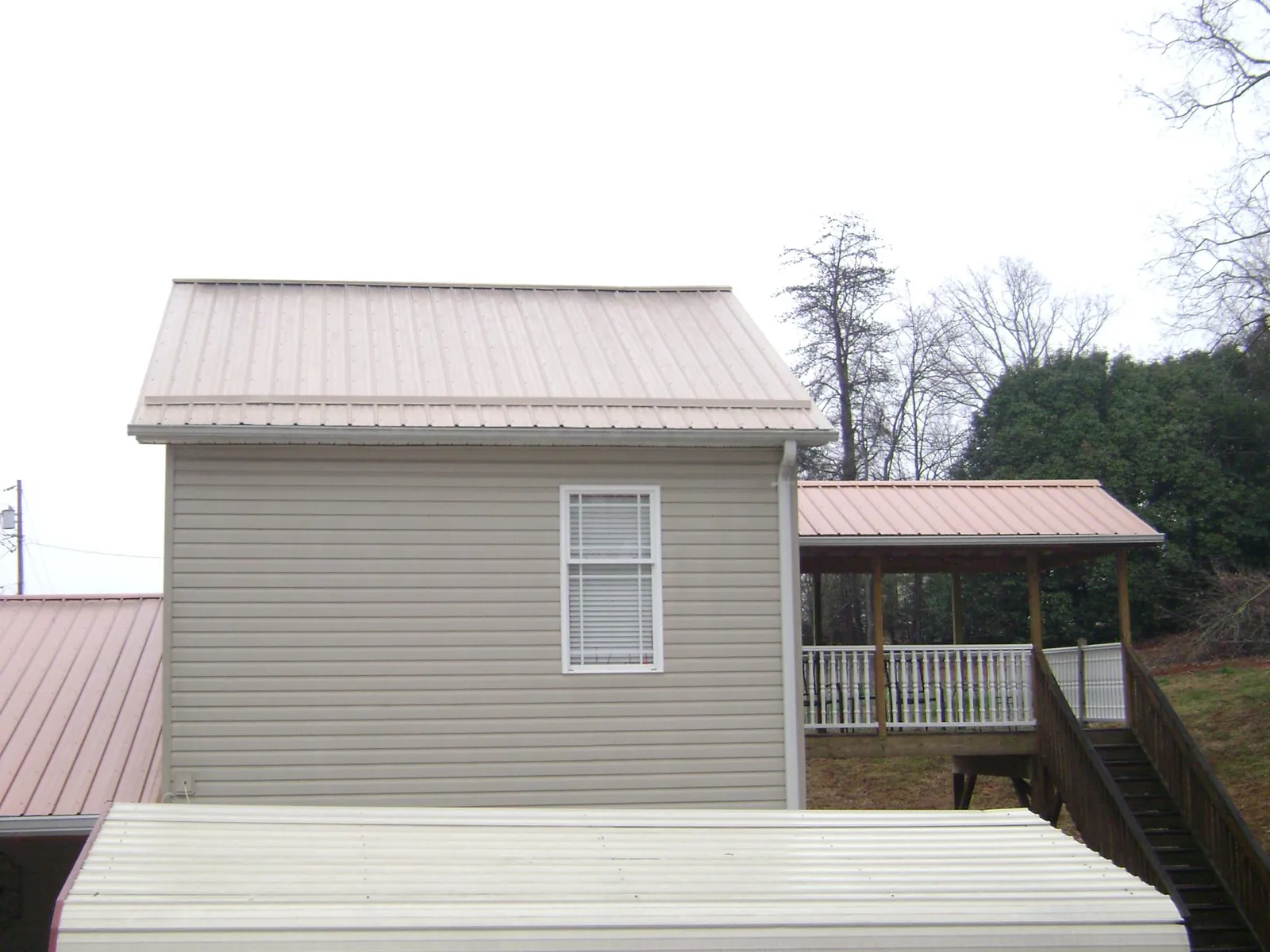 Tan metal roofs on a two story addition and attached porch, from a Roof Replacement job in Chinquapin